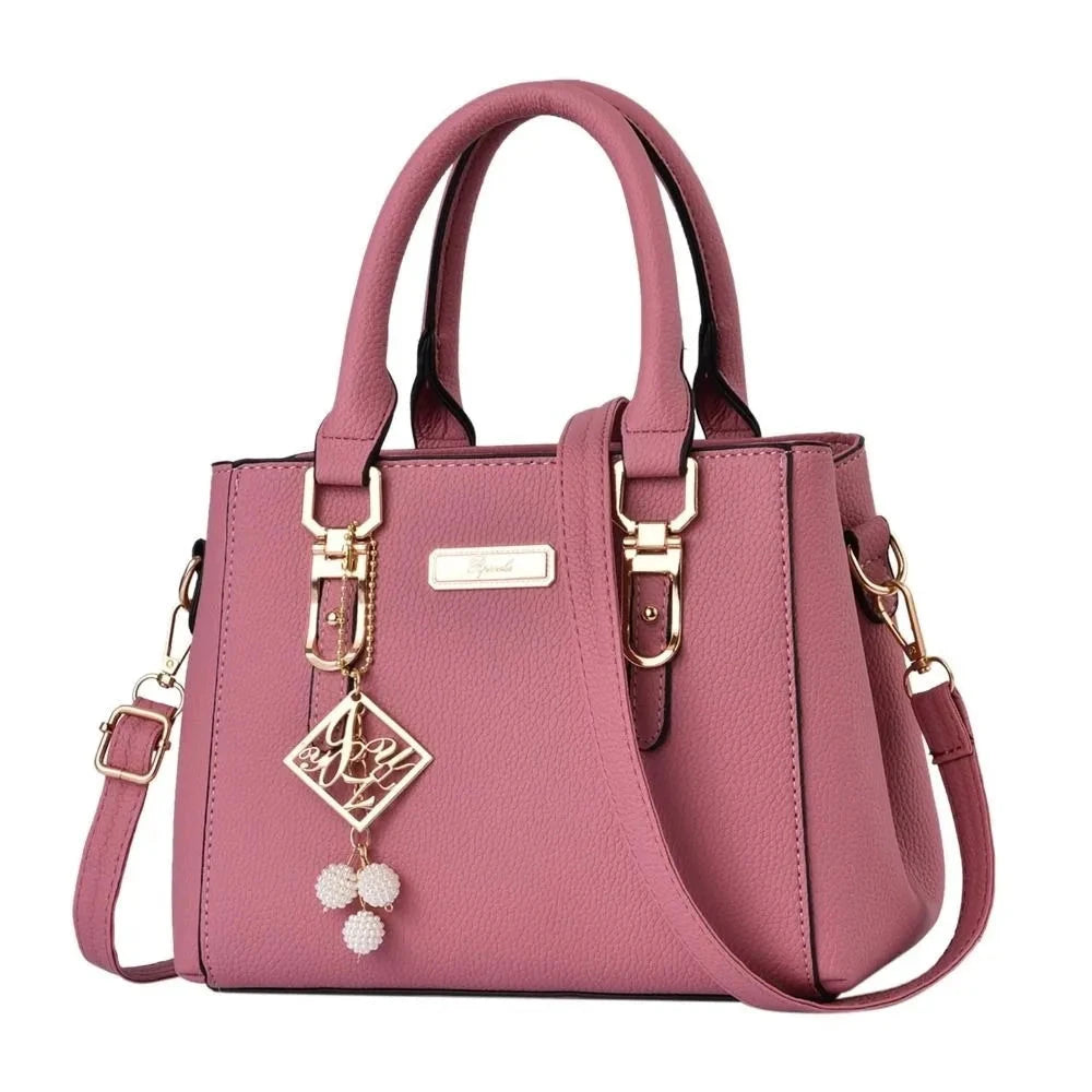 Pink handbag with gold accents and a decorative charm on a white background