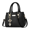 A black pebbled faux-leather handbag with double top handles, a detachable shoulder strap, gold-tone hardware, and a decorative hanging charm with white pearl-like beads, shown on a plain white background.