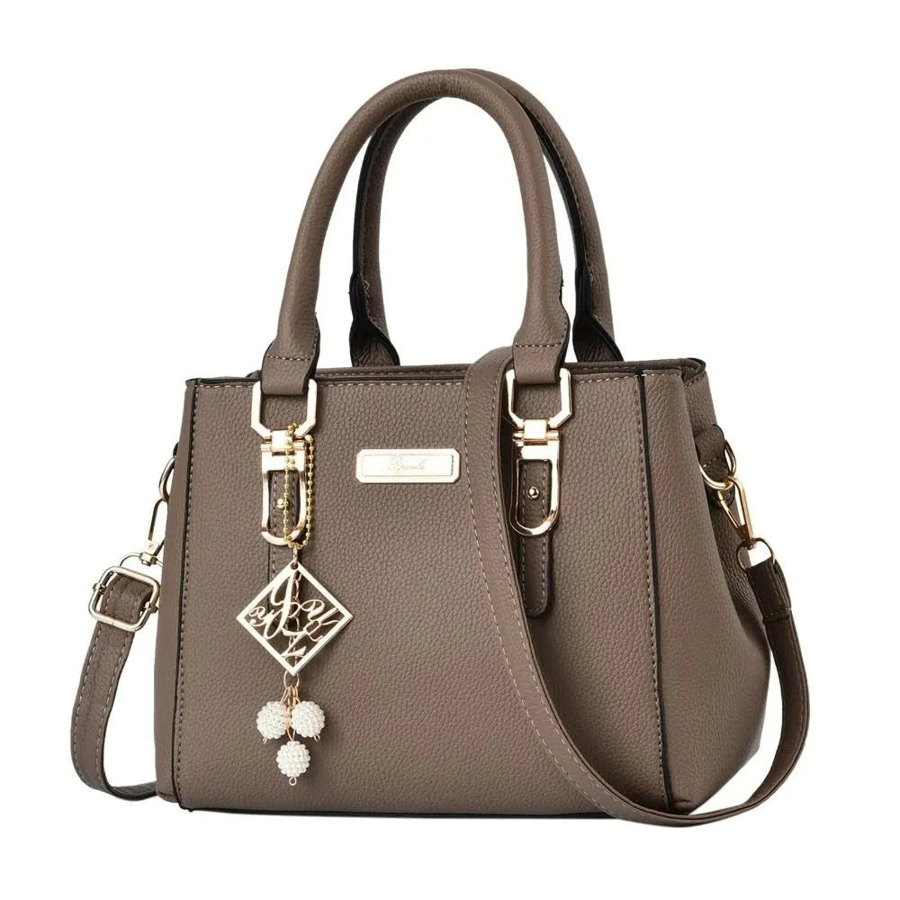 Brown handbag with decorative strap and pendant on a white background