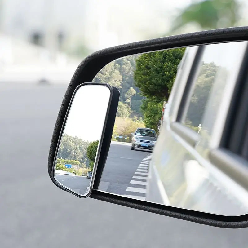 Car side mirror reflecting a road with trees and another vehicle.