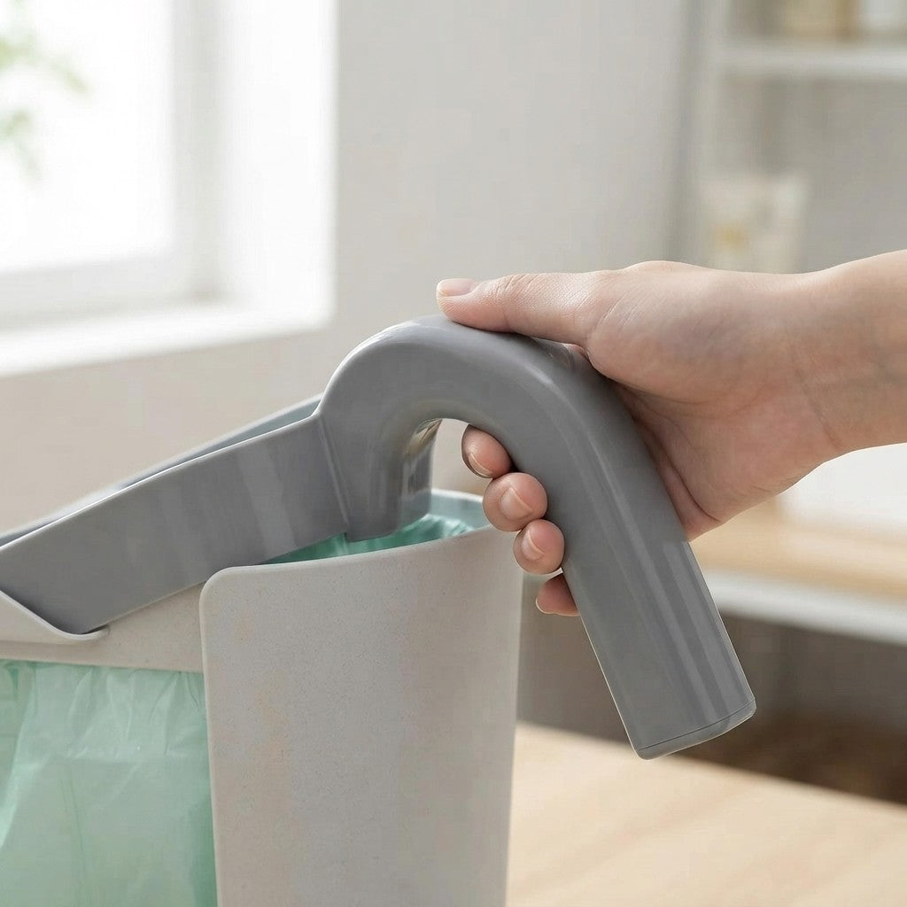 A hand holding a gray plastic handle attached to a white trash can, with a light green liner inside, in a softly blurred indoor setting.