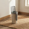 A modern automatic cat litter box in beige and gray, shown on a woven jute rug in a sunlit room corner.