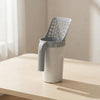 A modern white and gray plastic canister with a slotted lid, standing on a light wood table in a softly lit indoor setting.