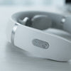 Close-up of a white and silver neck massager showing the control buttons on the headband, resting on a light gray surface.