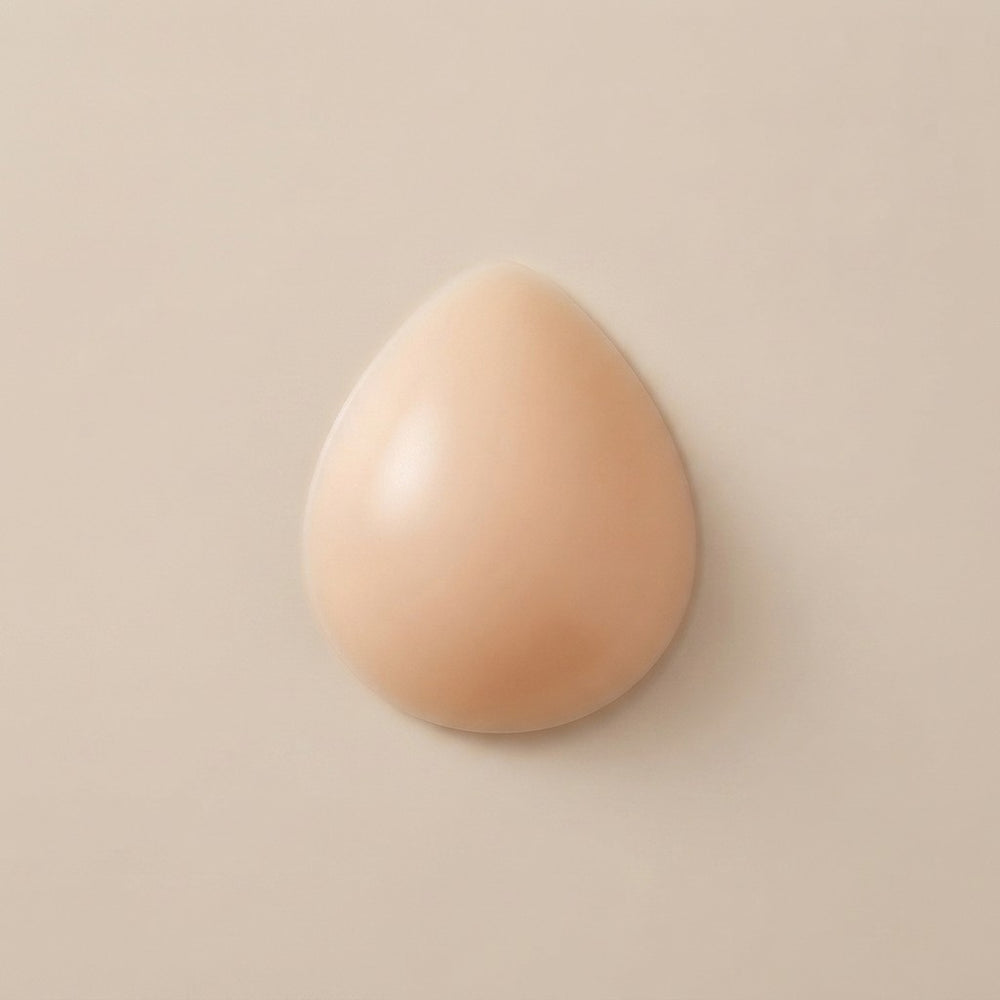 A teardrop-shaped beige makeup sponge or applicator with a smooth, matte finish, centered on a solid light beige background.